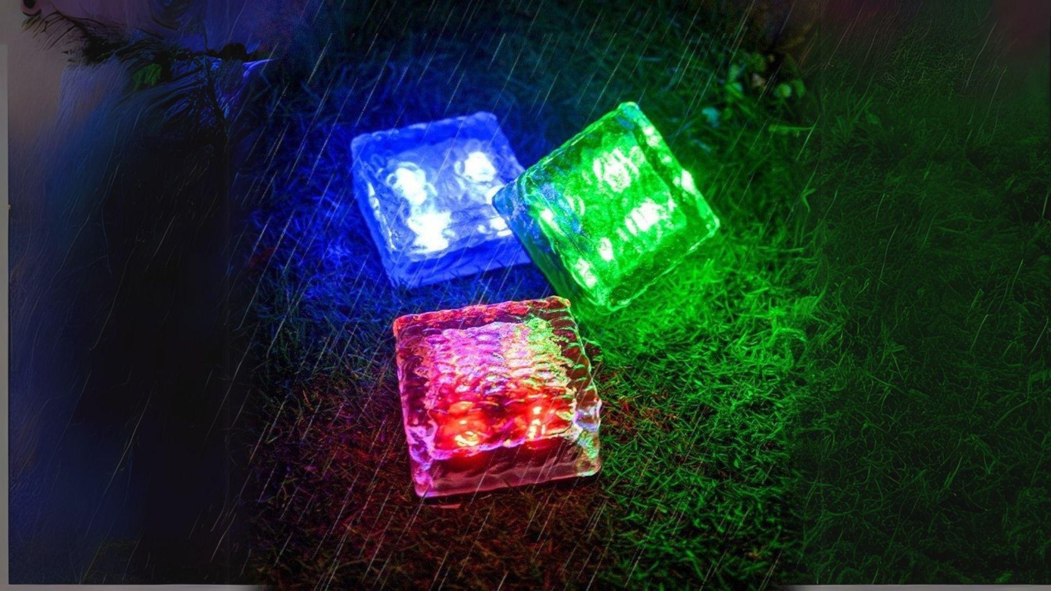 Solar Powered Ice Bricks Path Lights 6 Pack glowing red, blue, and green on wet grass at night.