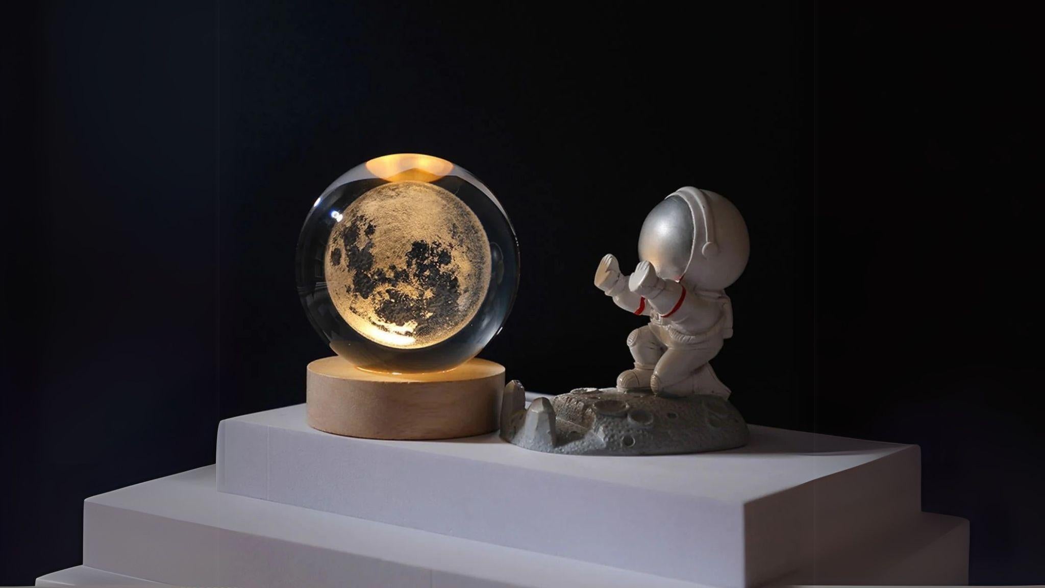 3D Solar System Crystal Ball Light displaying a glowing galaxy pattern on a wooden base beside an astronaut figurine.