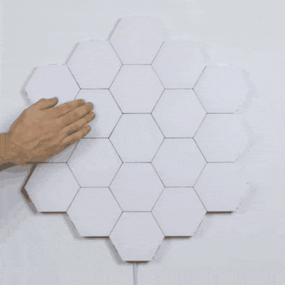 Modular touch-sensitive hexagon wall light panels with a hand touching one of the panels.