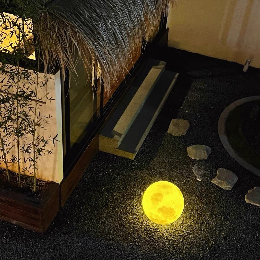 3D Moon Indoor & Outdoor Floor Lamp glowing warmly on outdoor gravel patio near steps at night
