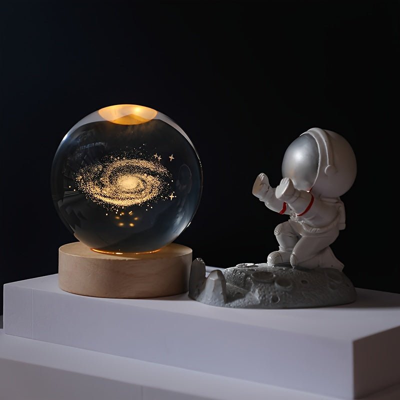 3D Solar System Crystal Ball Light displaying a glowing galaxy pattern on a wooden base beside an astronaut figurine.