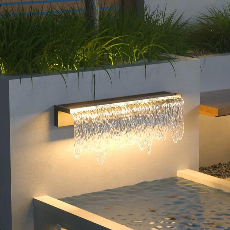 Acrylic Waterfall Outdoor Light casting elegant, flowing illumination over a modern garden wall at night.