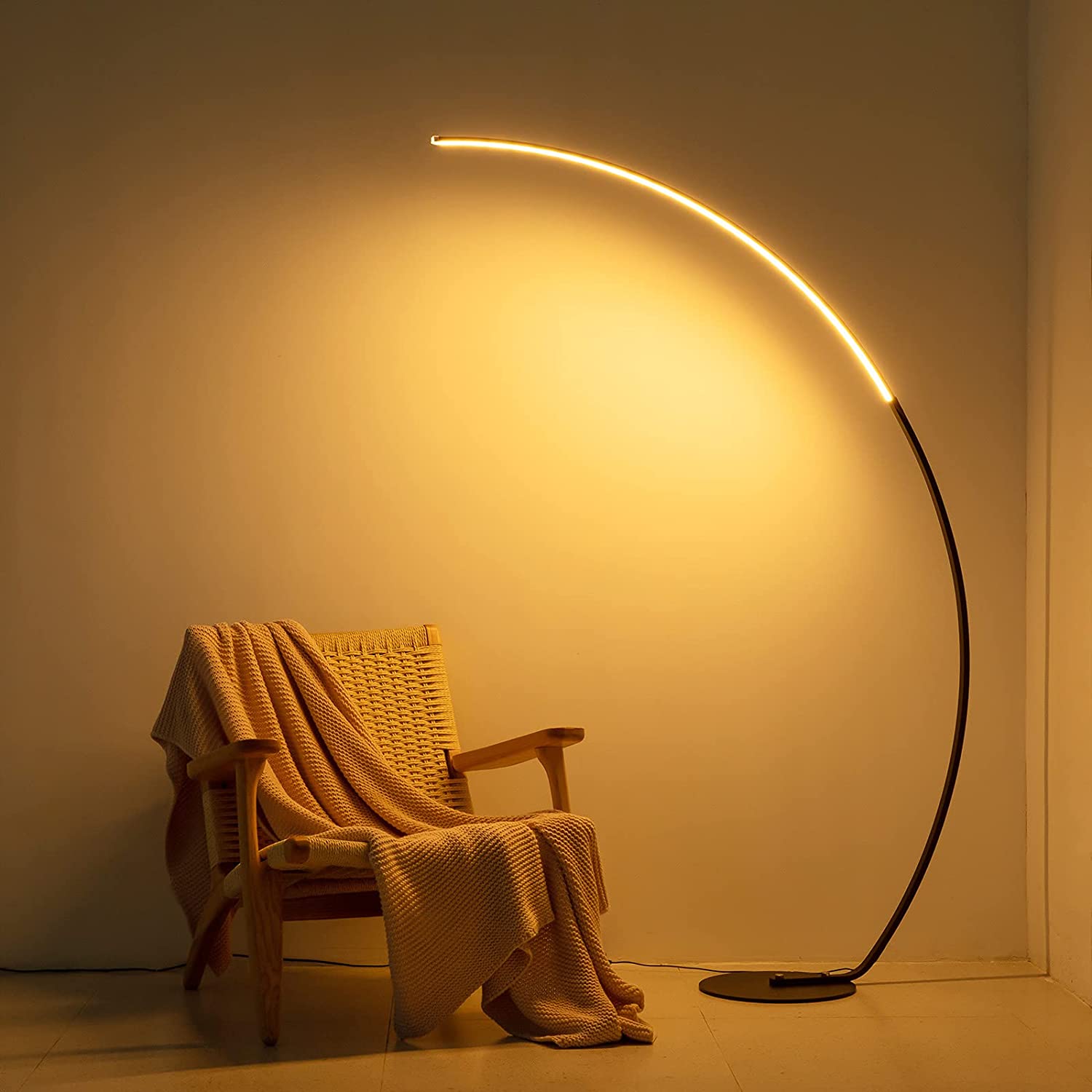 RGBW Modern Curve Floor Lamp casting warm LED light over cozy chair with a blanket in a minimalist room.