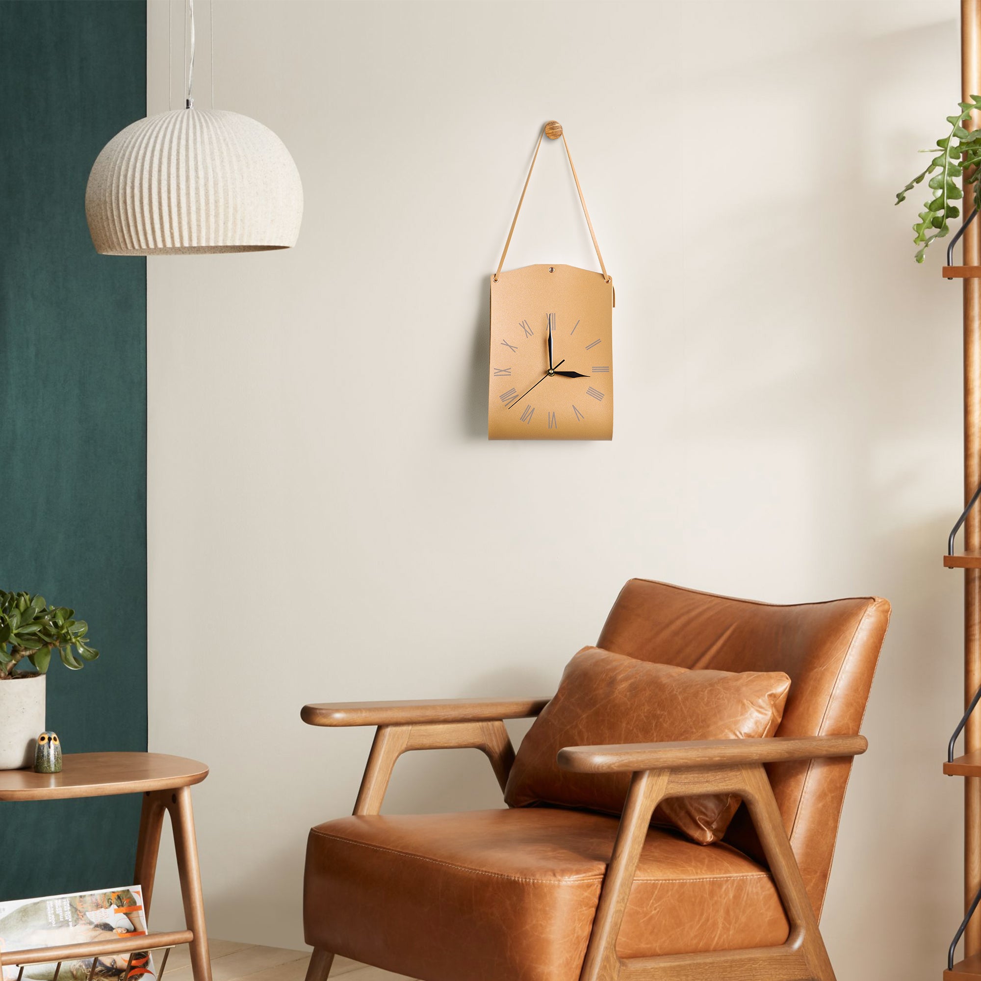 Roman Numerals Leather Wall Clock hanging on wall above a leather armchair in a stylish living room setting.