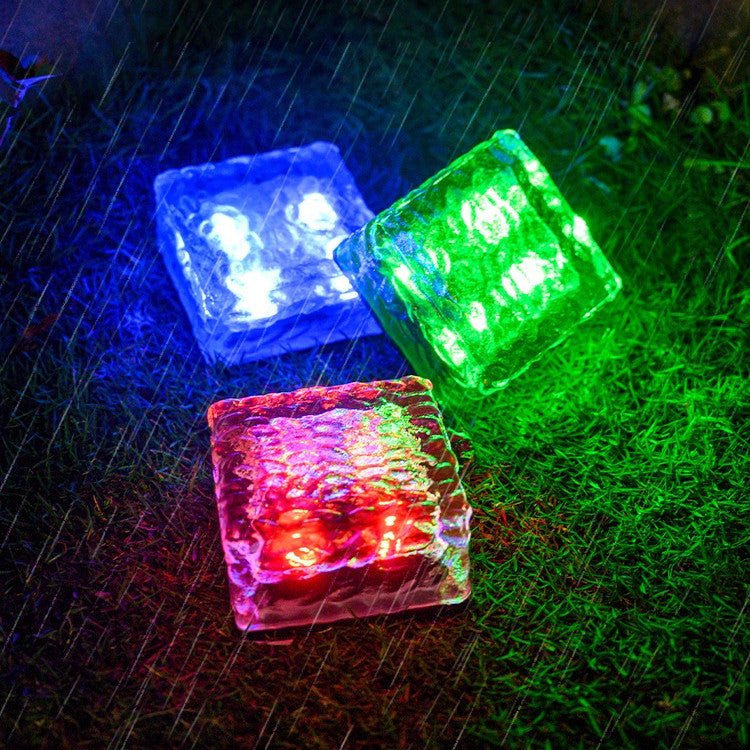 Solar Powered Ice Bricks Path Lights 6 Pack glowing red, blue, and green on wet grass at night.