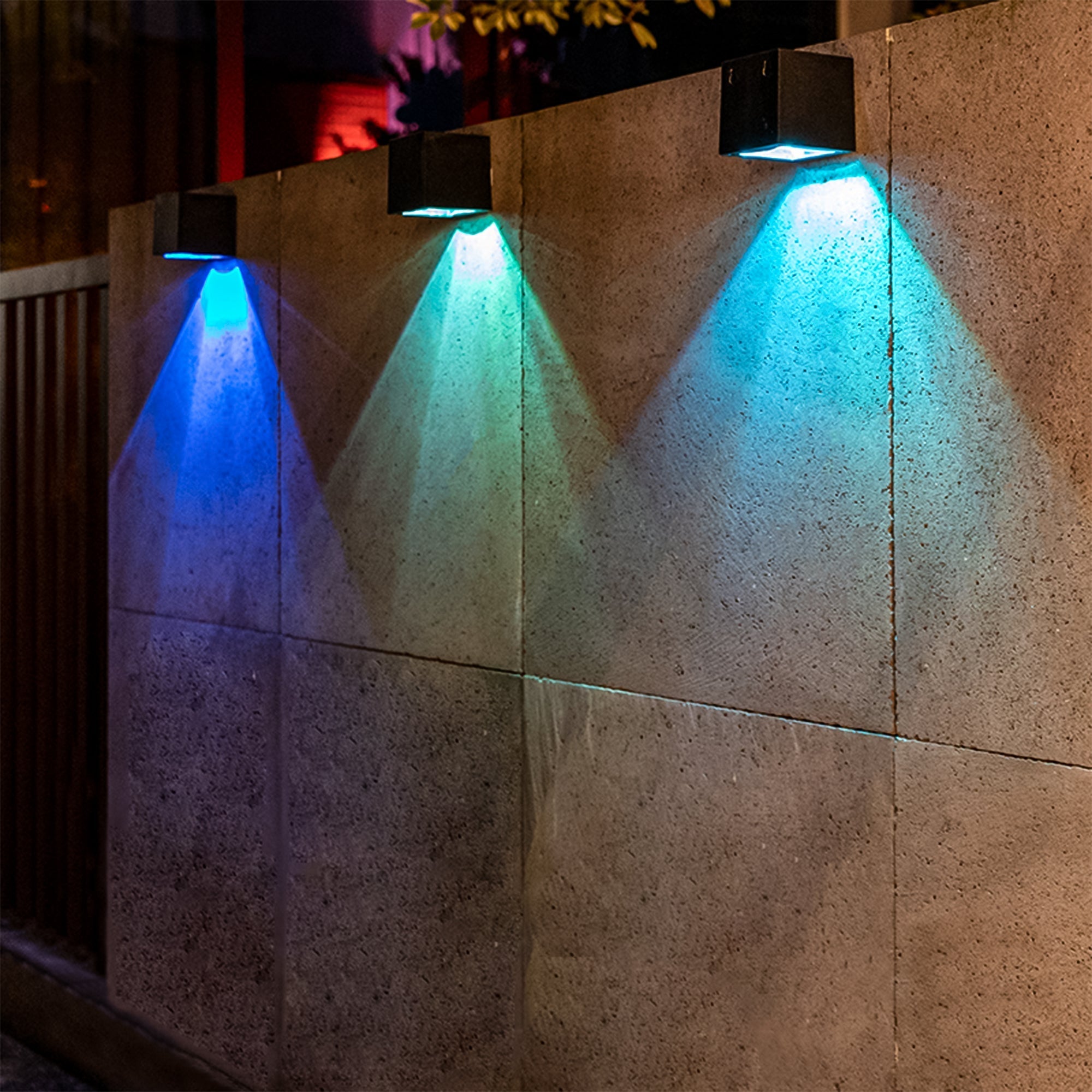 Solar Powered Outdoor Landscape Wall Lights illuminating a garden wall with vibrant blue and teal hues at night.