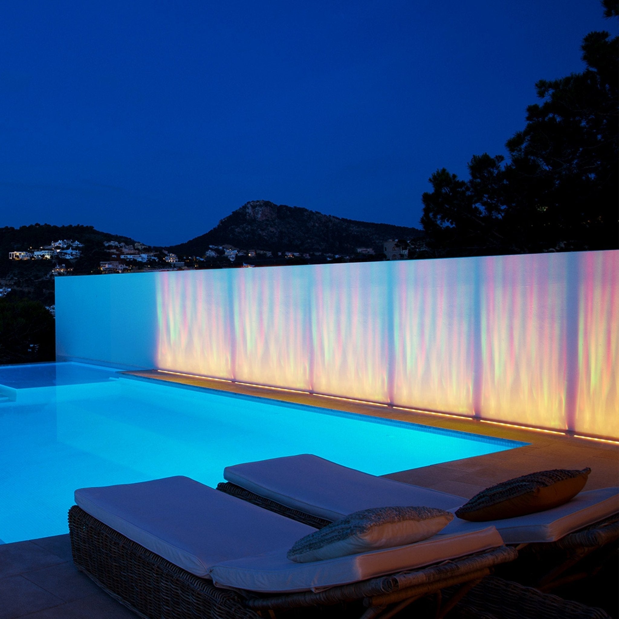 Waterproof Outdoor RGBW Ocean Wave Lights creating vibrant colorful waves along a modern poolside wall at night.