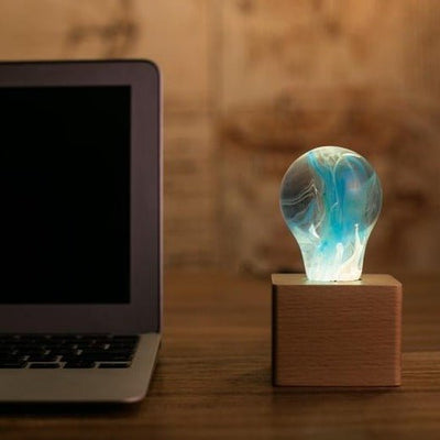 EP Light - Memory bulb glowing with unique blue swirl design on vintage wooden base beside laptop.