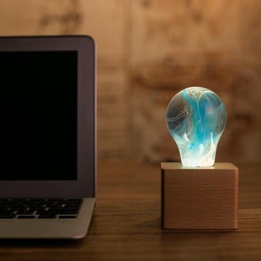 EP Light - Memory bulb glowing with unique blue swirl design on vintage wooden base beside laptop.