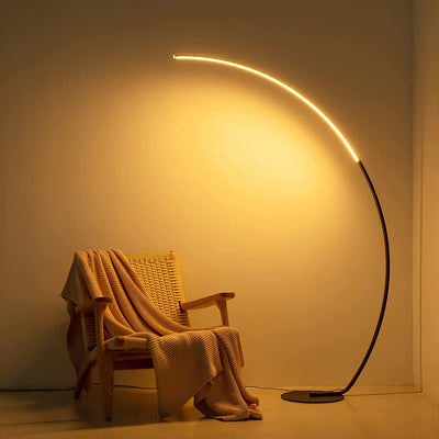 RGBW Modern Curve Floor Lamp casting warm LED light over cozy chair with a blanket in a minimalist room.